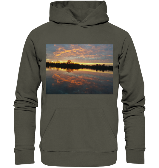 Der See am Abend - Organic Basic Hoodie von Silbers Magic Shop ist ein khakifarbener, nachhaltiger Hoodie, der das Bild einer ruhigen Seeszene mit einem leuchtenden Sonnenuntergang zeigt. Der Himmel zeigt Orange-, Gelb- und Lilatöne, die sich wunderschön im ruhigen Wasser spiegeln. Dieser Hoodie aus recyceltem Polyester und Bio-Baumwolle verfügt über eine Beuteltasche auf der Vorderseite und eine Kapuze mit Kordelzug.